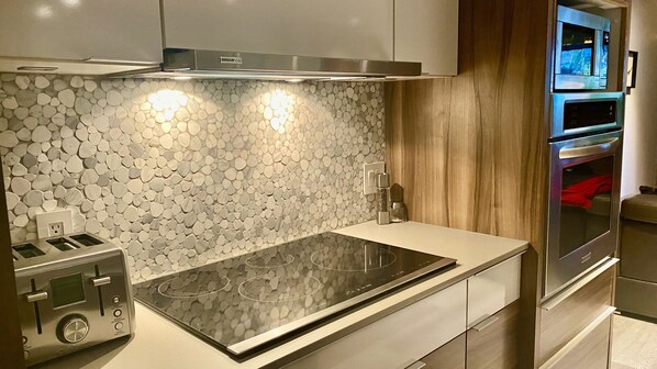 A modern kitchen with a stone backsplash, stainless steel appliances, and a built-in oven. - Zen2 Stylish Modern/Rustic Apartment in the Heart of Nature (Saint-Zénon)