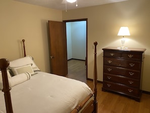 Una camera da letto con un letto a baldacchino, un comò in legno con cassetti e una porta che dà su un'altra stanza.