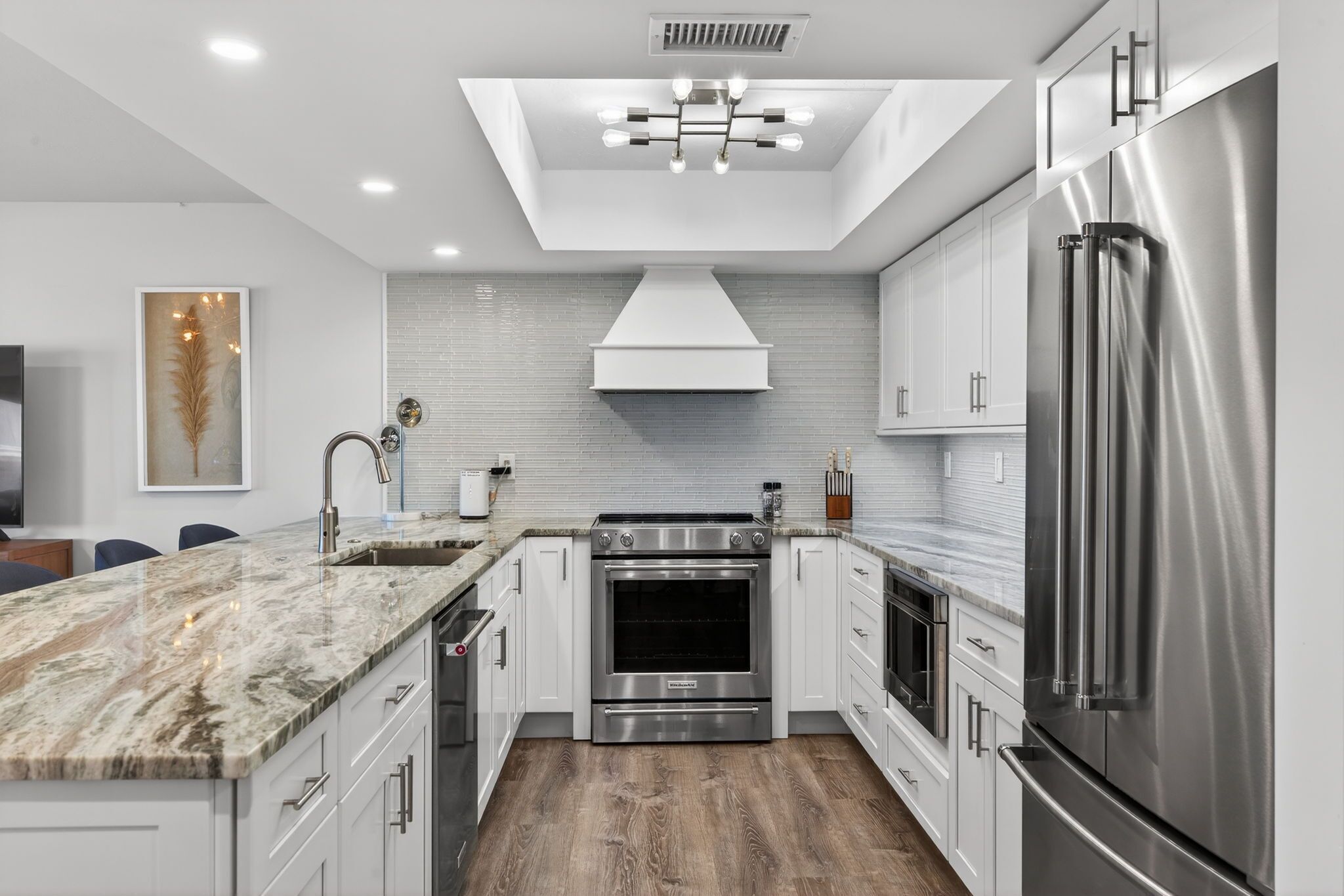 A modern kitchen with white cabinets, stainless steel appliances, and a marble countertop.