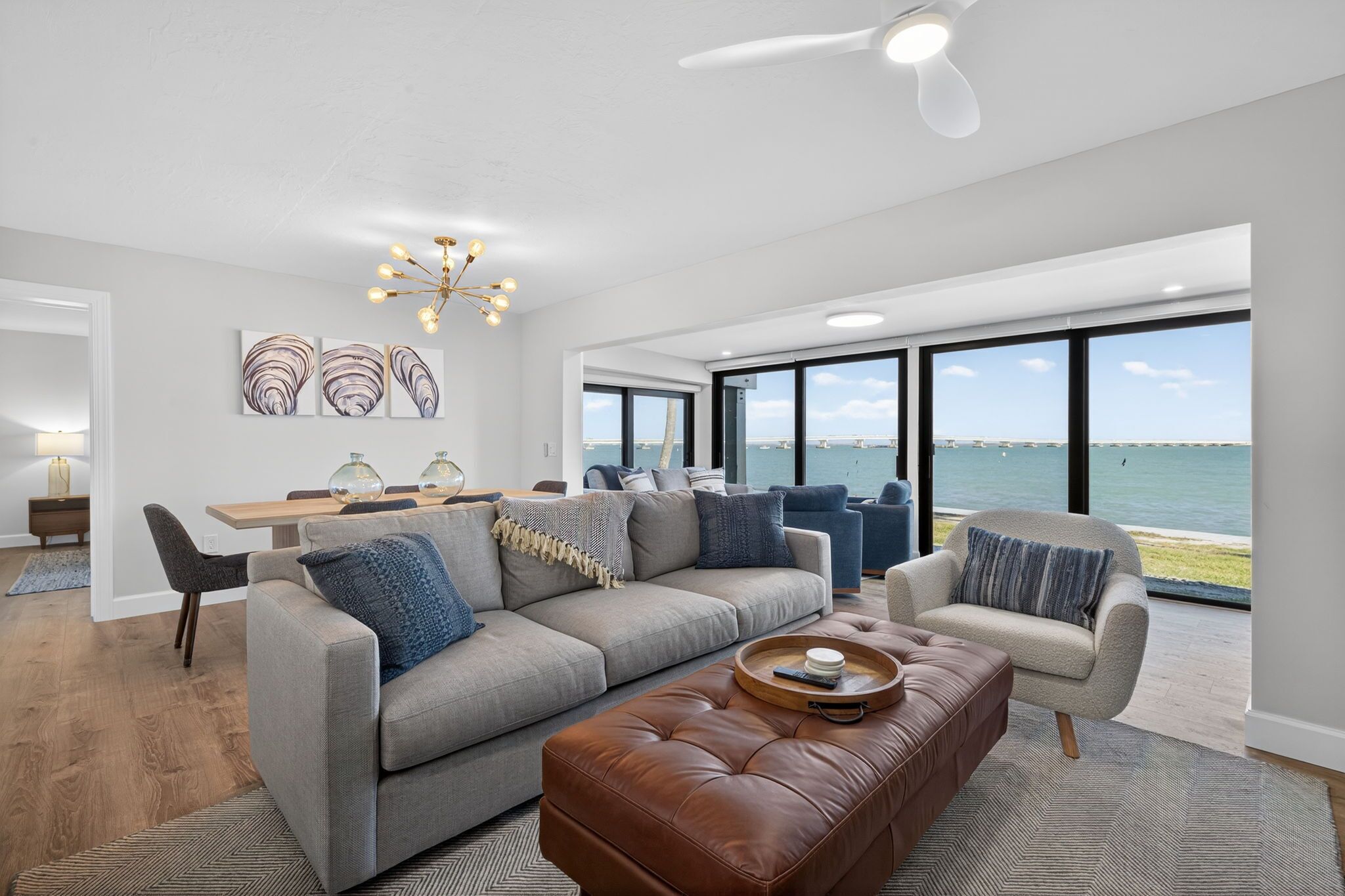 A modern living room with a large window overlooking a body of water, a dining area with a wooden table, and a cozy seating arrangement.