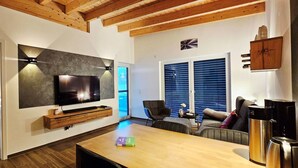A modern living room with a flat-screen TV, wooden furniture, and a coffee machine.