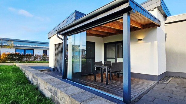 A modern house with a glass-enclosed patio, a wooden deck, and a view of a neighboring building.