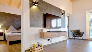 A modern living room with a flat-screen TV mounted on a wall, a wooden cabinet below, and a comfortable chair.