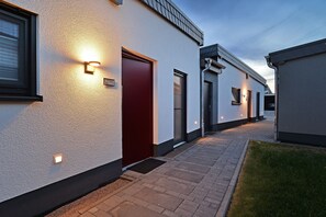 A modern building with a red door, a small window, and a light fixture on the wall.