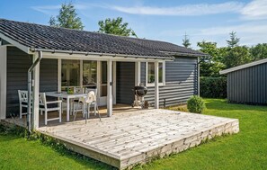Une petite maison avec un porche abrité, un barbecue et une table à manger avec des chaises.
