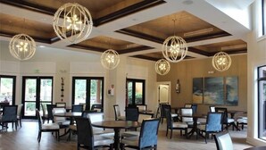 Uma sala de jantar ampla, com mesas e cadeiras redondas, grandes janelas e luminárias esféricas decorativas.