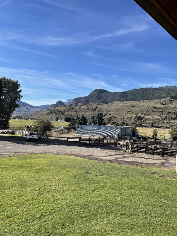 A fenced outdoor area with a building, a white car, and a mountain landscape. - Barnhouse at Slip & Slide Ranch (Gardiner)