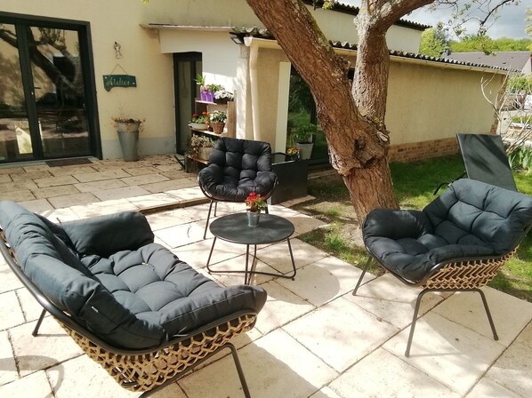 Un espace extérieur aménagé avec deux fauteuils confortables et une petite table, entouré de plantes en pot et d’un arbre.