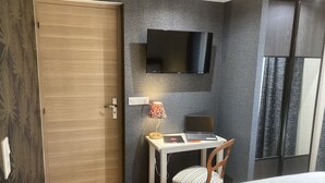 A bedroom with a wooden door, a desk with a laptop, a TV mounted on the wall, and a bed with a white duvet. - Le Clos des Feugrais*** - Quiet outbuilding (Saint-Aubin-lès-Elbeuf)
