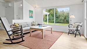 Un salon moderne comprenant un canapé, un fauteuil à bascule, une table basse et une grande fenêtre donnant sur un jardin.
