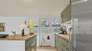 Une cuisine moderne avec des plans de travail en bois, un réfrigérateur en acier inoxydable et une vue à travers une porte vitrée.
