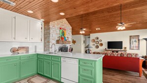 A kitchen with green cabinets, a dishwasher, and a stone wall. - Lake Travis Waterfront LUX/Dock/Firepit/Outdr play (Lago Vista)