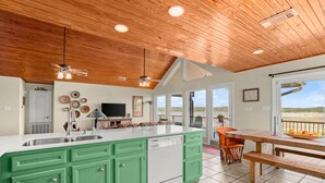 A kitchen with green cabinets, a dishwasher, and a large island. There is a dining area with a wooden table and chairs. - Lake Travis Waterfront LUX/Dock/Firepit/Outdr play (Lago Vista)