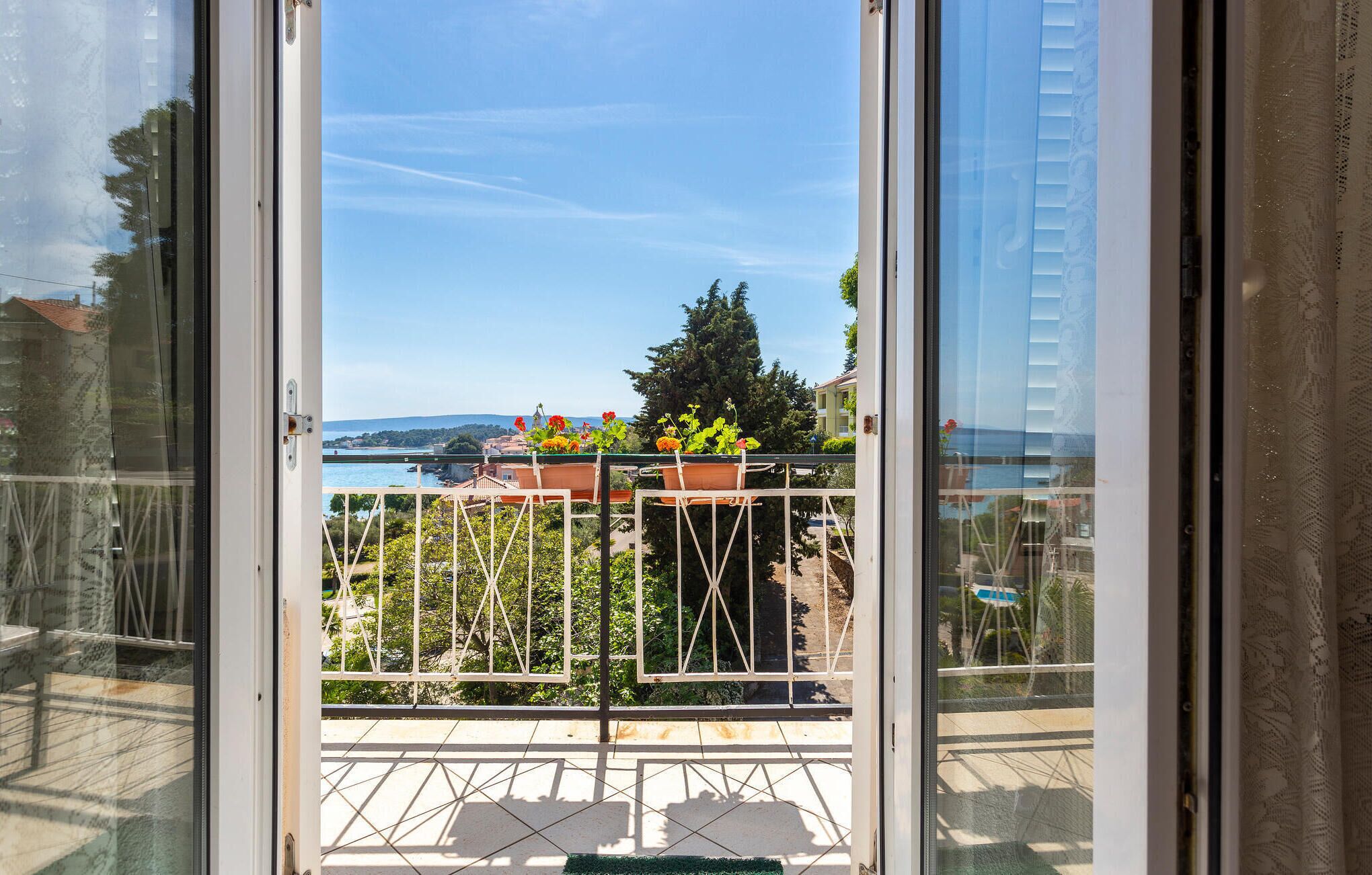 A balcony with a metal railing, potted plants, and a view of a body of water and distant hills.