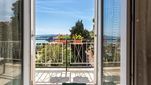 Un balcon doté d’une balustrade en métal, de plantes en pot et offrant une vue sur une étendue d’eau et des collines lointaines.
