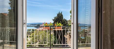 A balcony with a metal railing, potted plants, and a view of a body of water and distant hills.