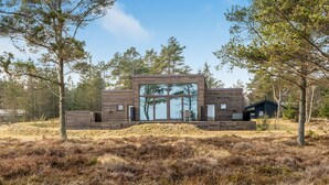 A modern cabin with large windows, surrounded by a natural landscape with trees and dry grass. - Stunning home in Hals with sauna (Hals)