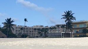 Ein Strand mit Sandküste, Palmen und einem Gebäudekomplex im Hintergrund.