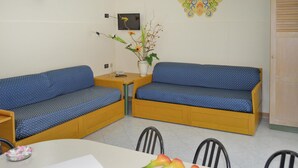 Ein Zimmer mit zwei blauen Sofas mit Muster, einem kleinen Holztisch, einer Vase mit Blumen und einer Wanddekoration.