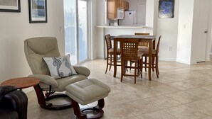 A spacious living room with a beige sofa, a blue rug, and a dining area with wooden chairs and a table. - Courtyard Villa with gas golf cart located between two Town Squares! (The Villages)