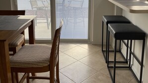 A dining area with a table and chairs, a sliding glass door leading to a balcony, and a small kitchen counter. - Courtyard Villa with gas golf cart located between two Town Squares! (The Villages)
