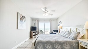Une chambre à coucher comprenant un lit, un ventilateur de plafond, une télévision, une chaise, une table de chevet et une fenêtre donnant sur un beau paysage.
