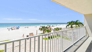 Une vue sur la plage depuis un balcon doté d’une balustrade blanche, avec des palmiers et un ciel dégagé.