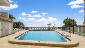 Une piscine rectangulaire dont la profondeur est indiquée à 6 pieds, entourée de chaises longues et de palmiers, avec un ciel bleu dégagé au-dessus.