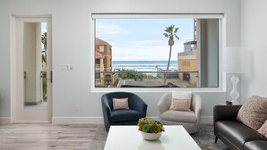 A modern living room with a large window overlooking a beach, two sofas, a coffee table with a plant, and a white lamp.