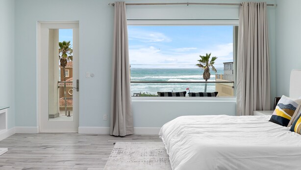 A bedroom with a large window, a bed, a ceiling fan, and a view of the ocean.