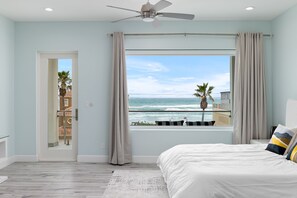 Een slaapkamer met een groot raam, een bed, een plafondventilator en uitzicht op de oceaan.