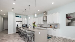 A modern kitchen with a central island, bar stools, white cabinetry, and pendant lighting.