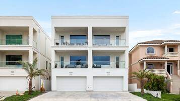 A modern multi-story residential building with a central garage, balconies, and a well-maintained lawn.