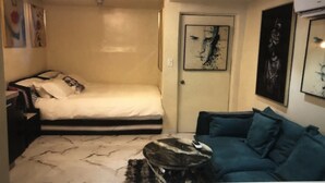 Ein kleiner, gemütlicher Raum mit einem Bett, einem blauen Sofa, einem kleinen Tisch und einer Tür.