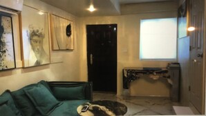 Ein Wohnzimmer mit einem grünen Sofa, einem Couchtisch und einem Fernseher. Im Hintergrund sind eine Tür und ein Fenster zu sehen.