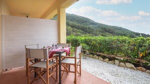 A covered patio with a table set for two, overlooking a lush, green hillside. - 1 bedroom beach front apartment in Nisportino (Nisportino)