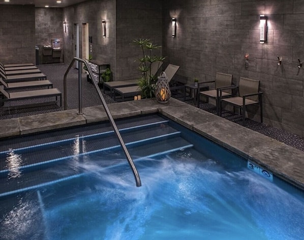A swimming pool with a metal ladder, lounge chairs, and a staircase leading to an upper level.