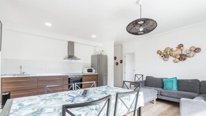 A modern kitchen with a central island, a dining area with a patterned tablecloth, and a living area with a gray sofa and decorative wall art. - Gorgeous apartment in Santa Pola with WiFi (Santa Pola)