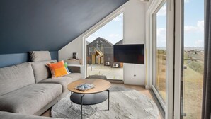 A modern living room with a grey sofa, a coffee table, and a large window offering a view of a building and the sea. - Luxurious apartment in Slagelse (Slagelse)