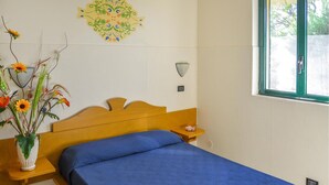Una cama con colcha azul, cabecera de madera y mesita de noche con un florero.