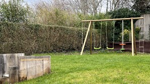 A backyard with a wooden swing set, a wooden fence, and a hedge. - Charming house on the Opal Coast, 5 minutes from the beach by car (Wimille)