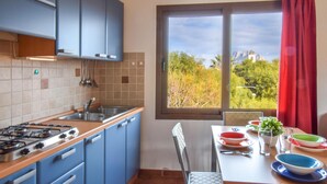 A kitchen with blue cabinets, a gas stove, a sink, and a window with a view of trees and a building.