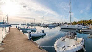 A marina with various boats docked, a concrete dock, and a calm water surface reflecting the sky.