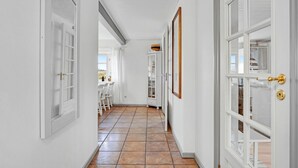 Un pasillo con puertas blancas, suelo de baldosas y vista a un comedor con mesa y sillas.