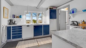 Una cocina moderna con armarios blancos y azules, un lavavajillas empotrado y un ventanal grande.