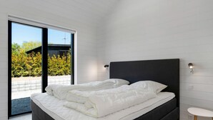 Quarto moderno com uma cama grande, uma mesinha de cabeceira e vista para o exterior através de uma porta de vidro deslizante.