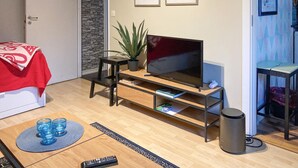 A living room with a TV, a plant, a bookshelf, a trash can, and a red blanket on a bed. - Lovely apartment in Borgholm with WiFi (Borgholm)