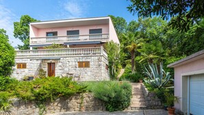 A two-story stone building with a balcony, surrounded by lush greenery and a garage. - Beach front apartment in Opatija with WiFi (Opatija)