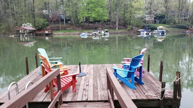 Une jetée en bois, agrémentée de chaises Adirondack aux couleurs vives, fait face à un lac paisible où flottent des bateaux.