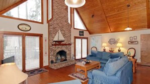 Un salon spacieux avec une cheminée en briques, un canapé bleu, un plancher en bois et de grandes fenêtres.